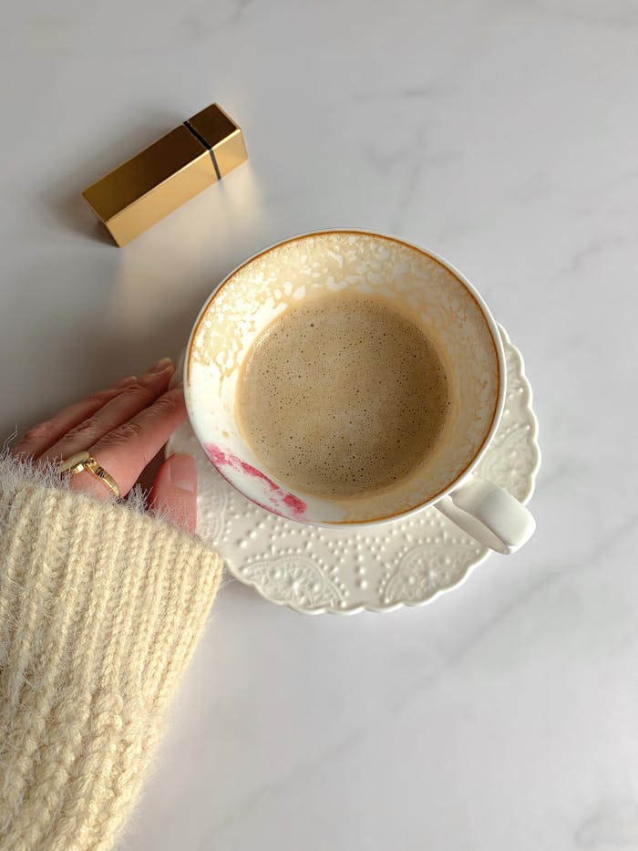A cozy scene with a ceramic cup of coffee on a white table, sweater, and lipstick mark.