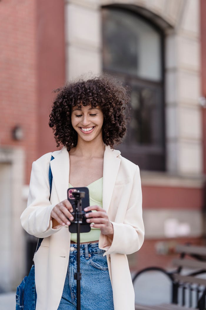 Stylish woman recording vlog on smartphone in a lively city street.